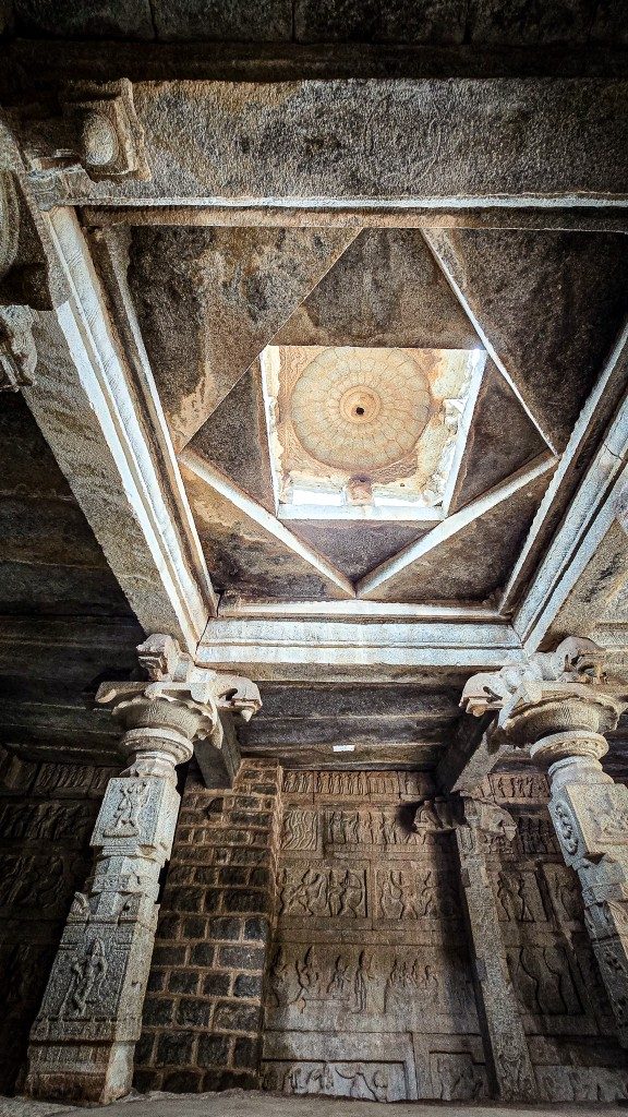 Looking directly upward at a star-pattern corbelled ceiling at a Hampi temple — layered stone forming a precise geometric composition