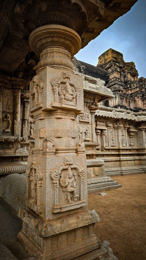 Wide view of a Hampi temple mandapa hall — carved pillars receding into depth, golden stone light