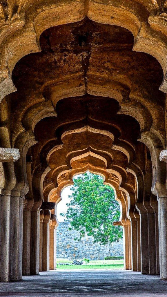 The cusped lotus-bud arches of the Lotus Mahal receding into depth — warm sandstone plaster, a tree framed at the end of the corridor