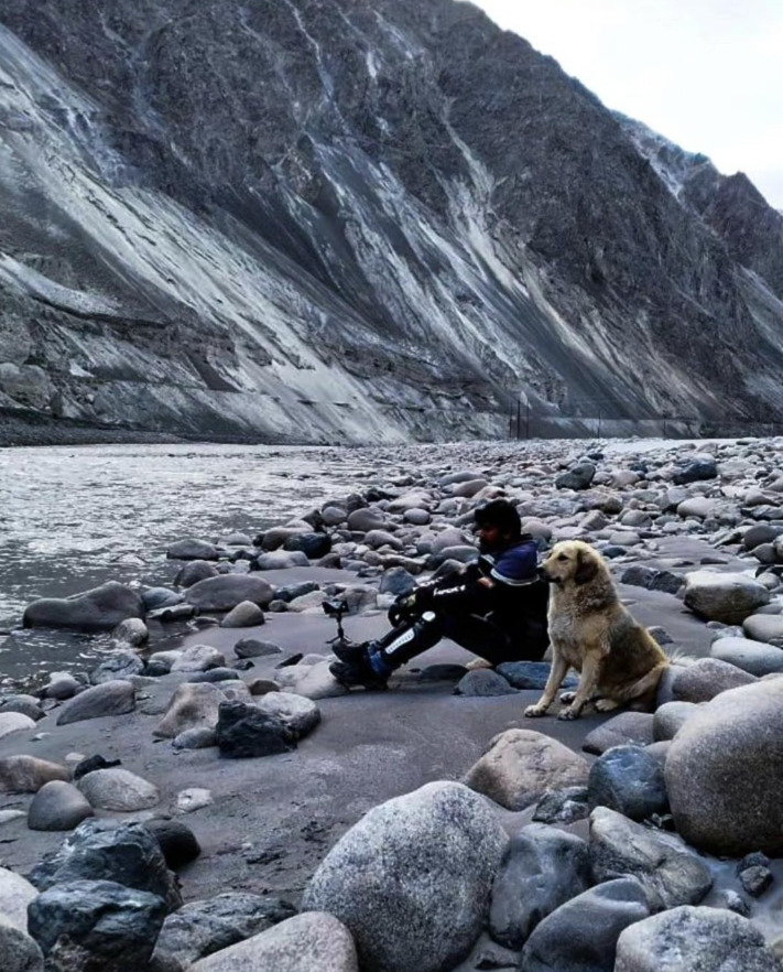 Traveller and a dog sitting beside a rocky mountain river in Ladakh