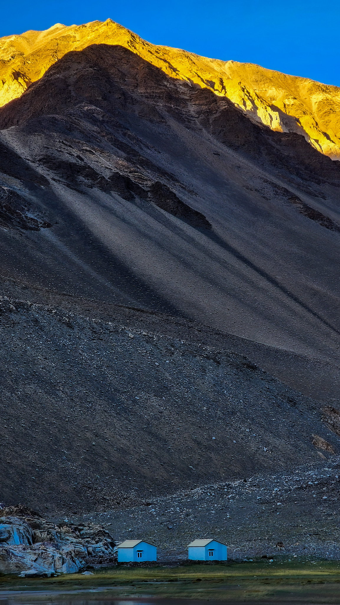 Two blue houses beneath a golden-lit mountain in Ladakh