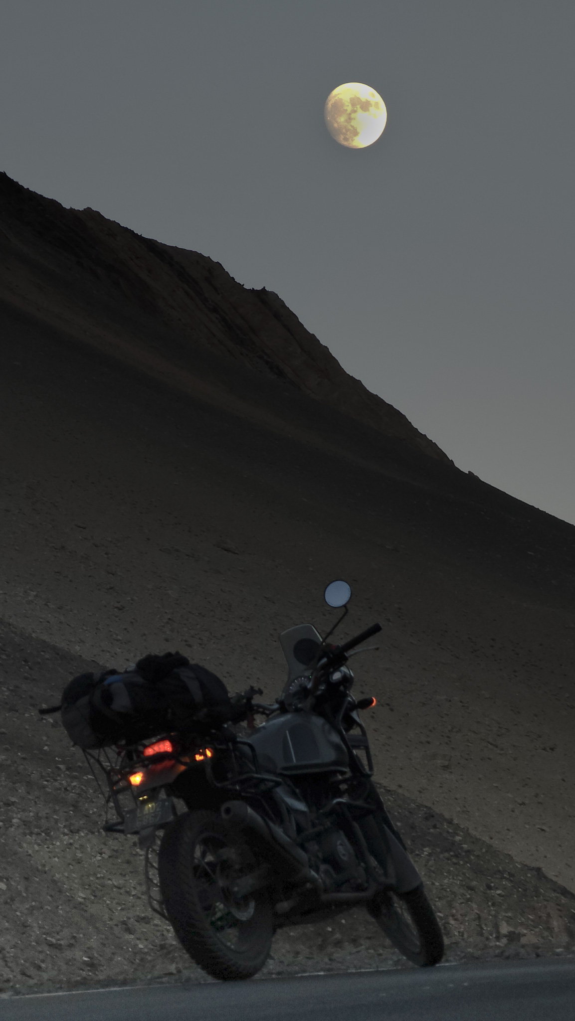 Moonrise over a motorcycle parked on a Ladakh mountain road at dusk
